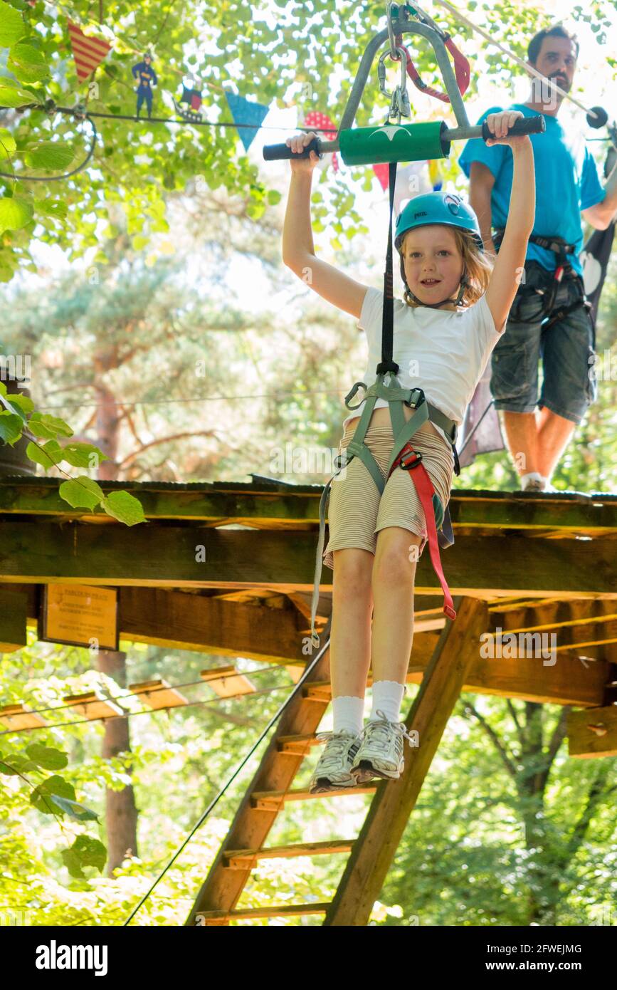 Young girl girls child kid on a children obstacle course zip wire line activity trail high in woodland forest tree, at an adventure park in France during the summer. Rather like a Go Ape adventure experience. (100) Stock Photo