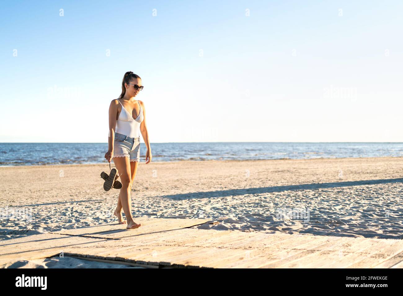 Thoughtful lonely woman walking at an empty beach. Thinking about life at the peaceful quiet sea. Pensive sad single girl leaving. Broken heart. Stock Photo