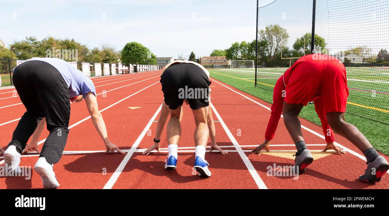 Rear view of three high school track sprinters in the set position at the starting line ready to run down the track in lanes. Stock Photo