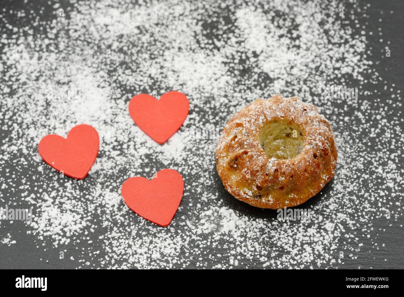 round cake with red heart and powdered sugar on black plate Stock Photo