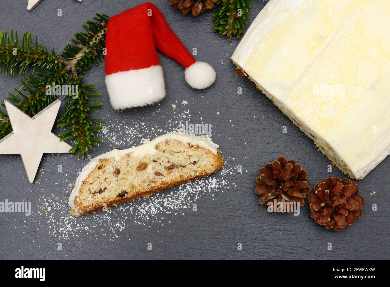 christmas stollen with fir branch, pine cone, stars  and santa hat lying on black shale at christmas time Stock Photo