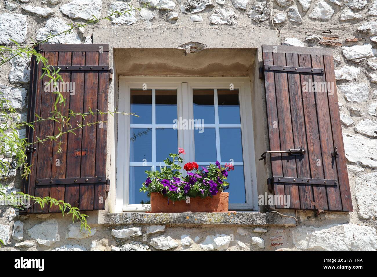 window with brown shutters and colorful flowers on the window sill Stock Photo