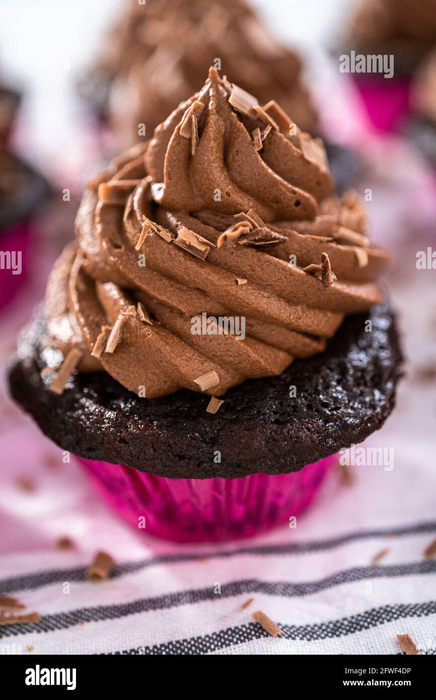 Piping chocolate ganache frosting on top of chocolate cupcakes Stock