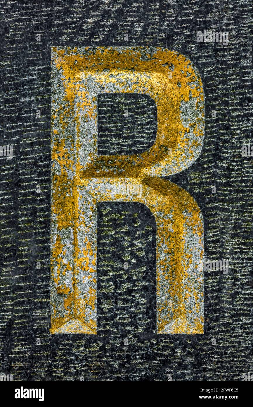 Golden weathered letter R on black granite Stock Photo