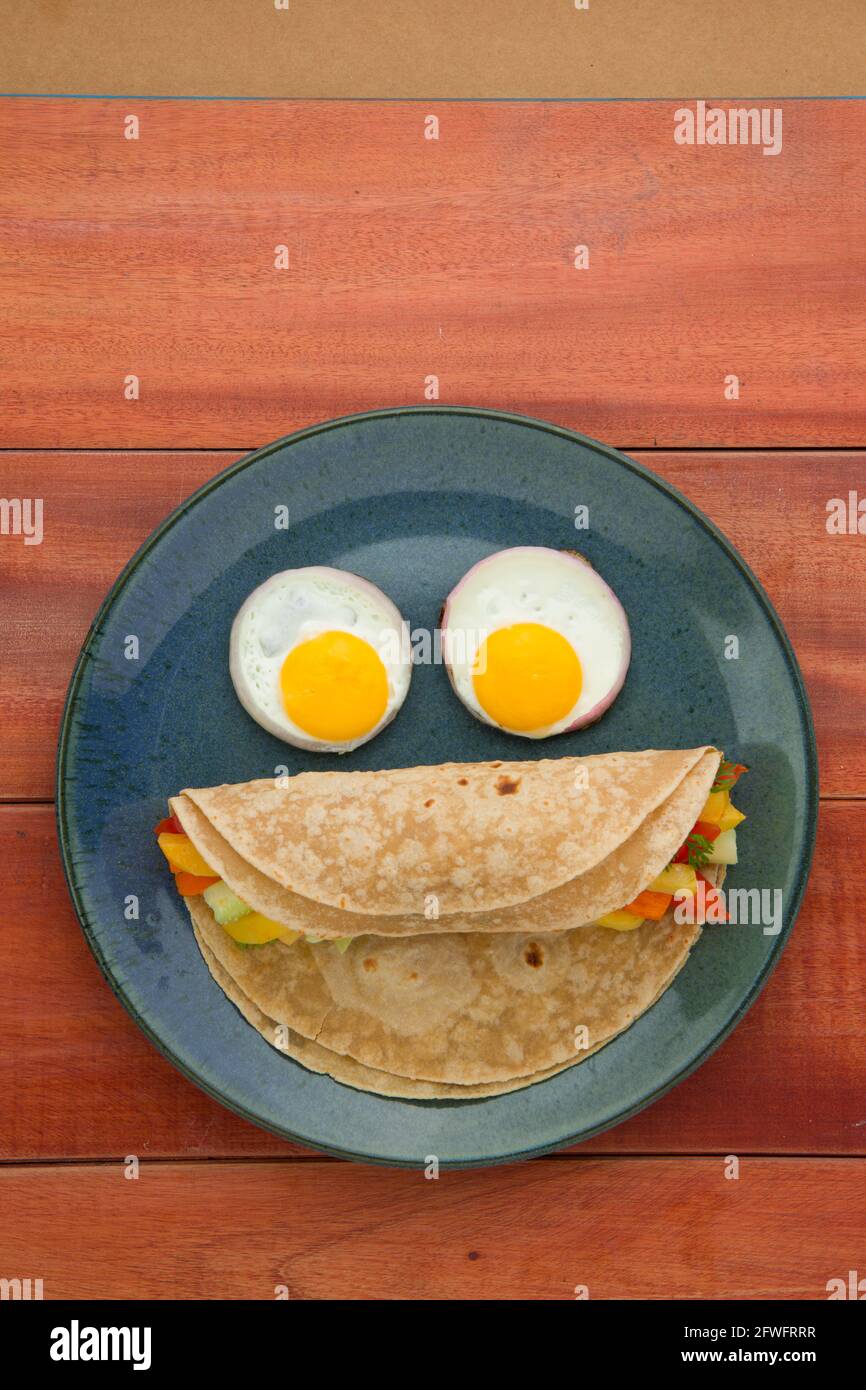 Smiley face food item chappati,healthy food made of wheat flour and it is stuffed with vegetables and eyes are made of half boiled eggs and it is arra Stock Photo