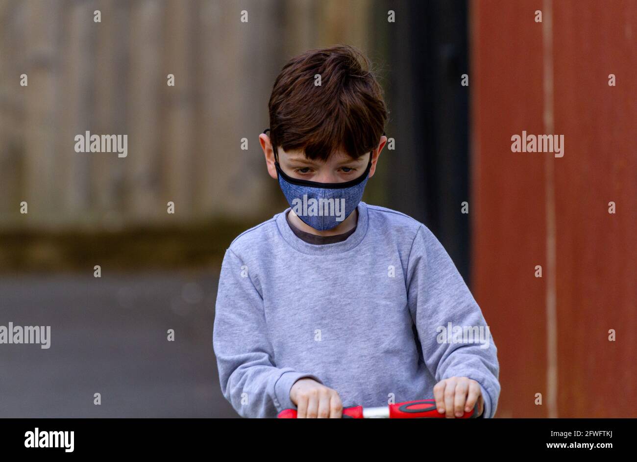 Portrait of a redhead boy wearing a face mask, riding a red scooter on ...