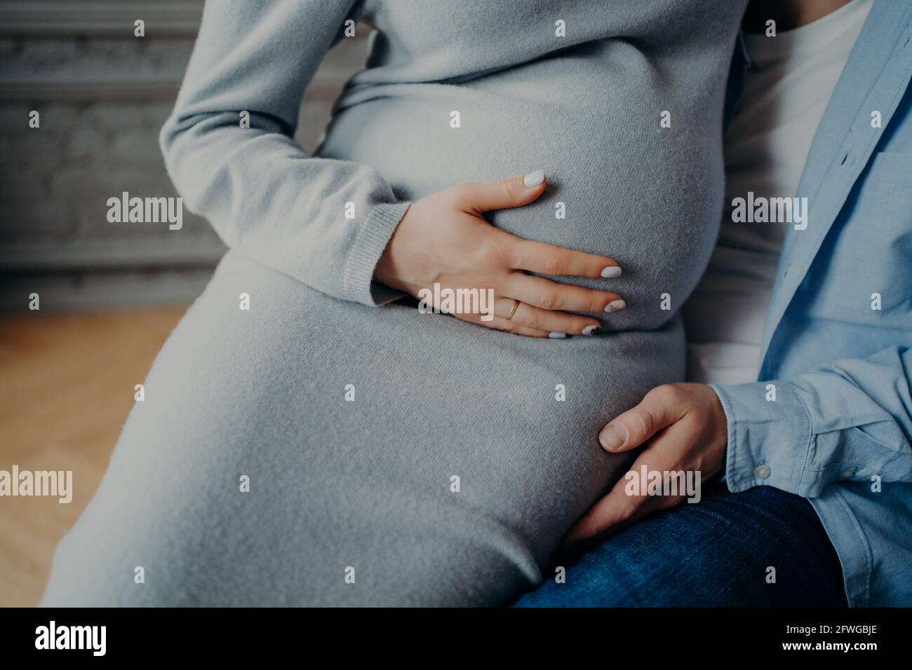 Pregnant woman with big belly poses on husbands hands feels child