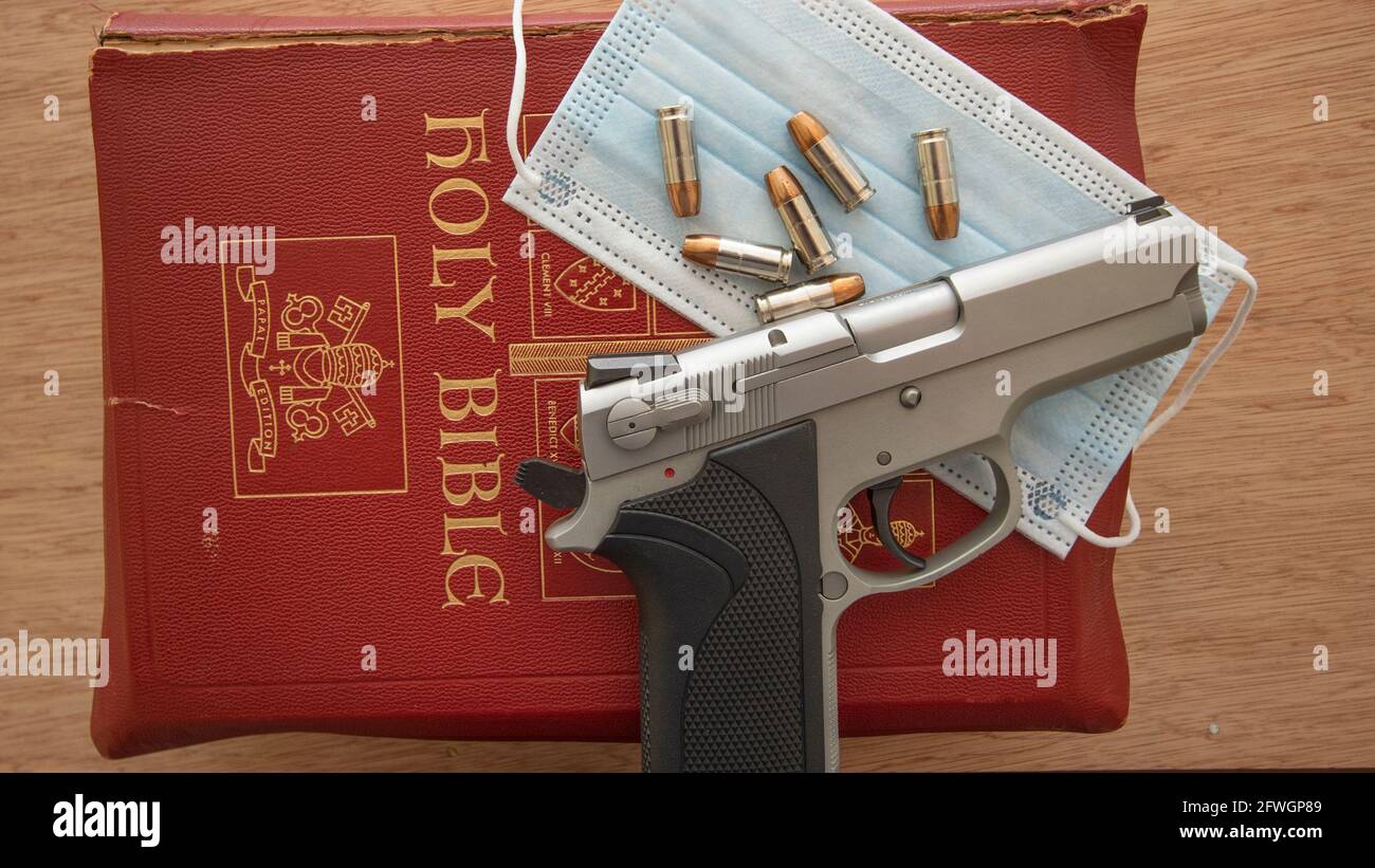 A gun resting on a bible with a Covid-19 protection mask and ammo Stock Photo