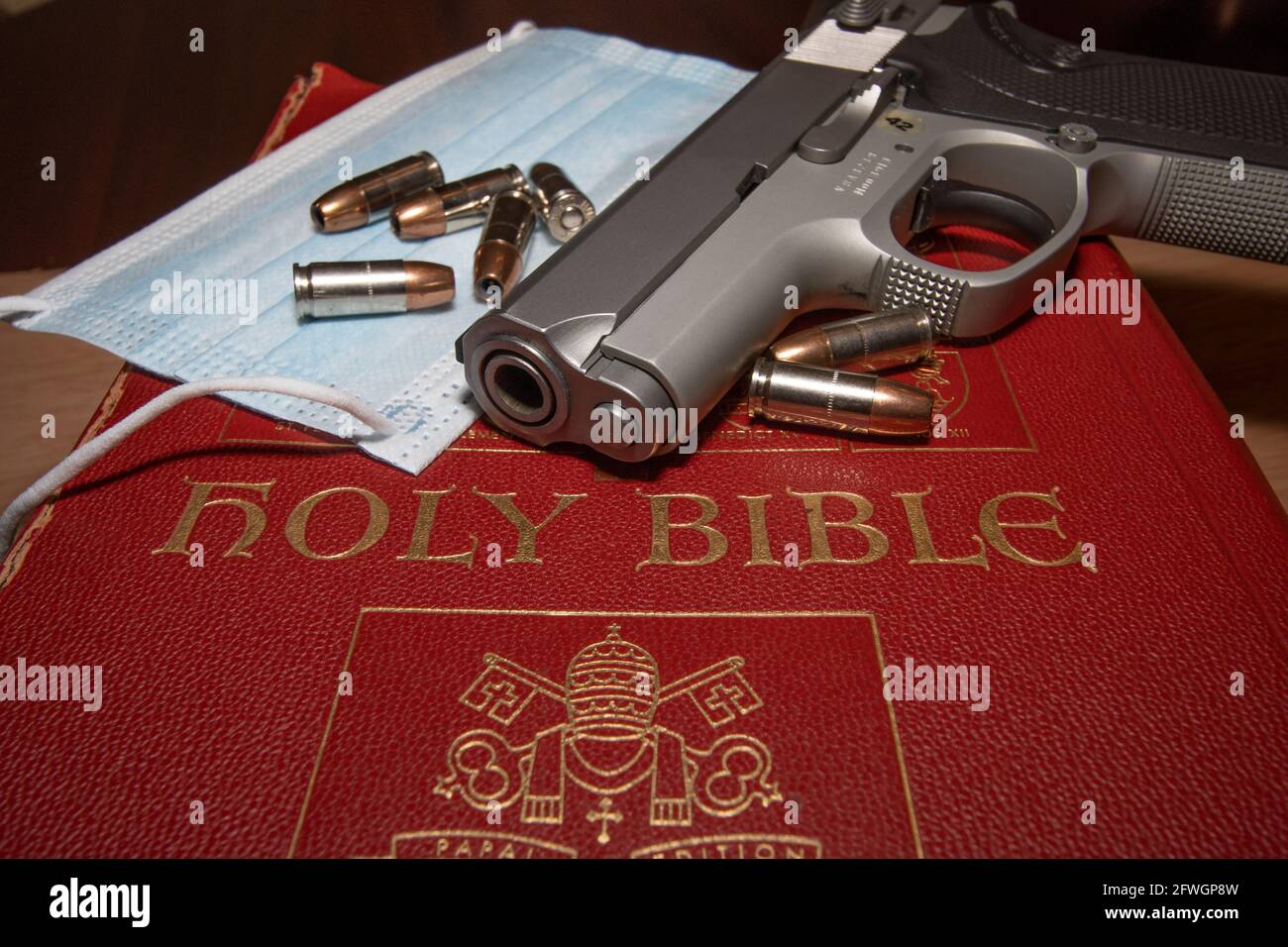 A gun resting on a bible with a Covid19 protection mask and ammo Stock