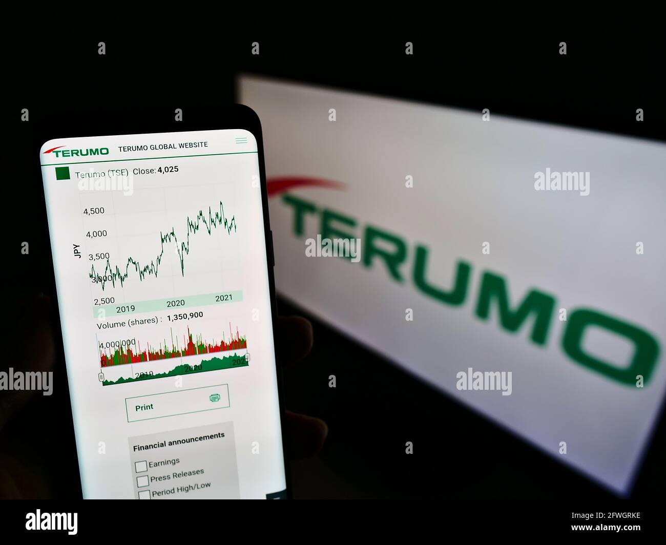 Person holding cellphone with webpage of Japanese medical equipment company Terumo Corp on screen in front of logo. Focus on center of phone display. Stock Photo