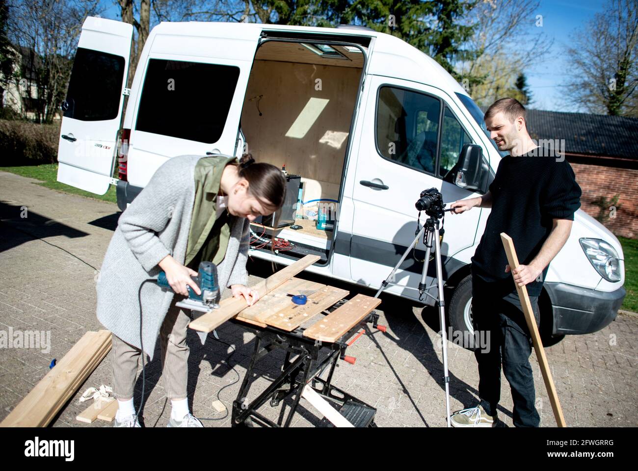 03 April 2021, Lower Saxony, Großenmeer: Greta Thomas and Hannes Wehrmann are cutting wood in front of their Mercedes-Benz Sprinter, which the couple is converting into a campervan. Photo: Hauke-Christian Dittrich/dpa Stock Photo