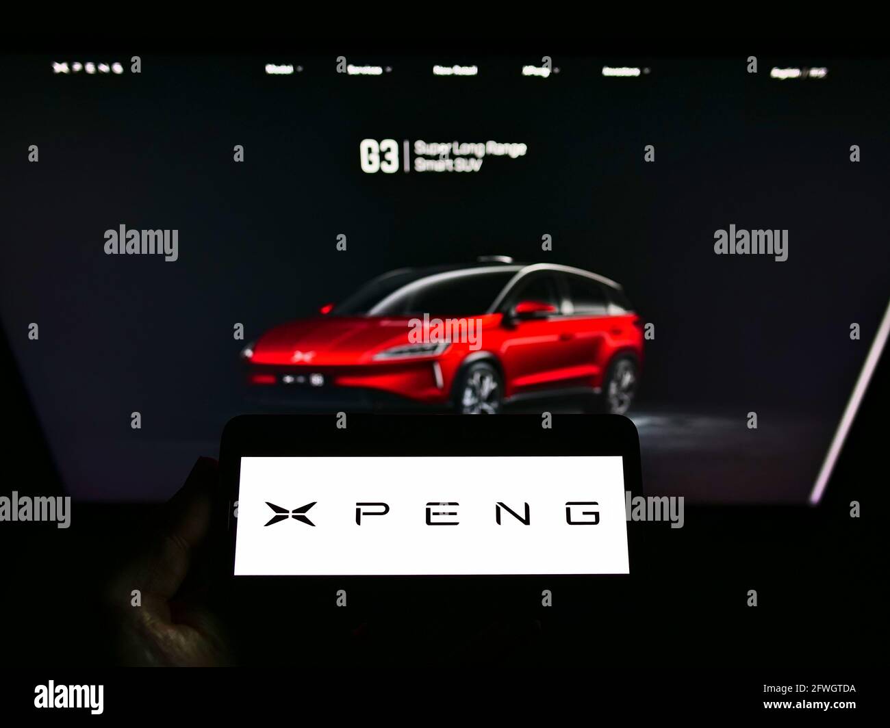 Person holding cellphone with logo of Chinese electric car manufacturer Xiaopeng Motors on screen in front of web page. Focus on phone display. Stock Photo