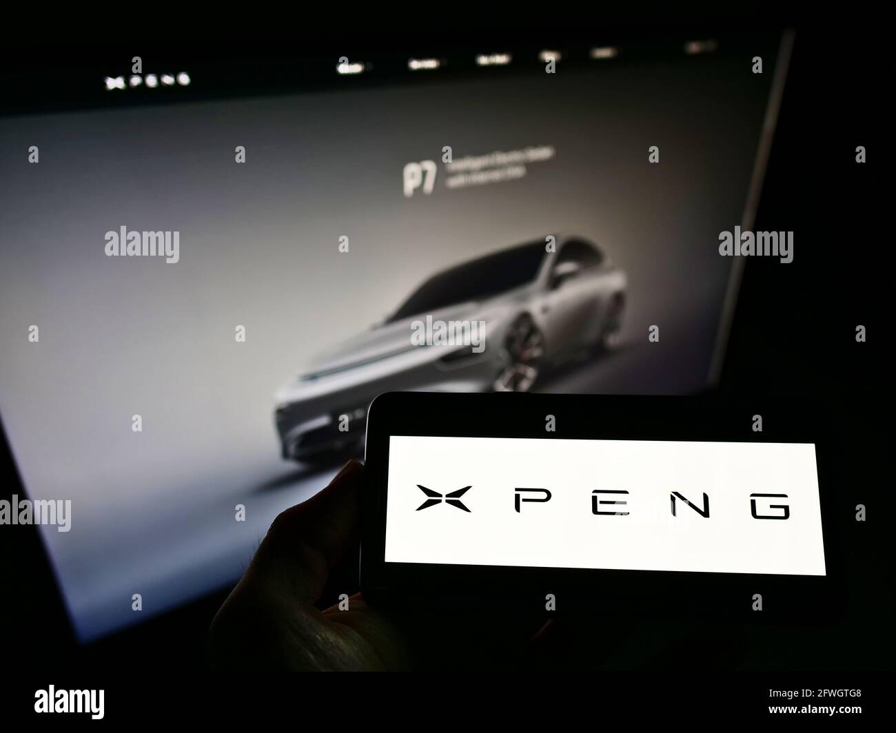 Person holding smartphone with logo of Chinese electric car manufacturer Xiaopeng Motors on screen in front of webpage. Focus on cellphone display. Stock Photo