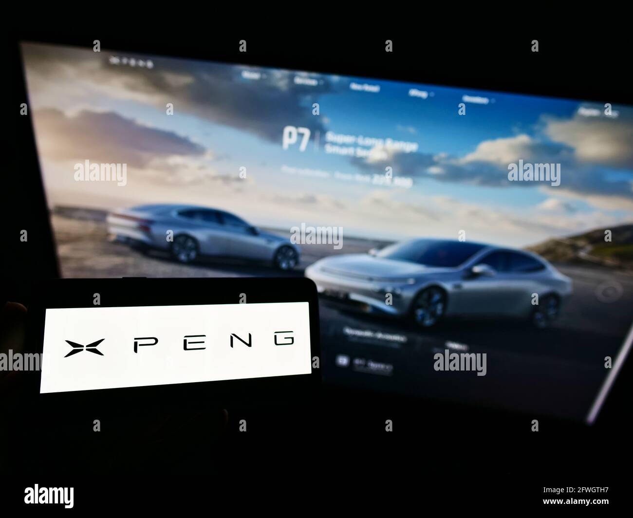 Person holding smartphone with logo of Chinese electric car manufacturer Xiaopeng Motors on screen in front of website. Focus on phone display. Stock Photo