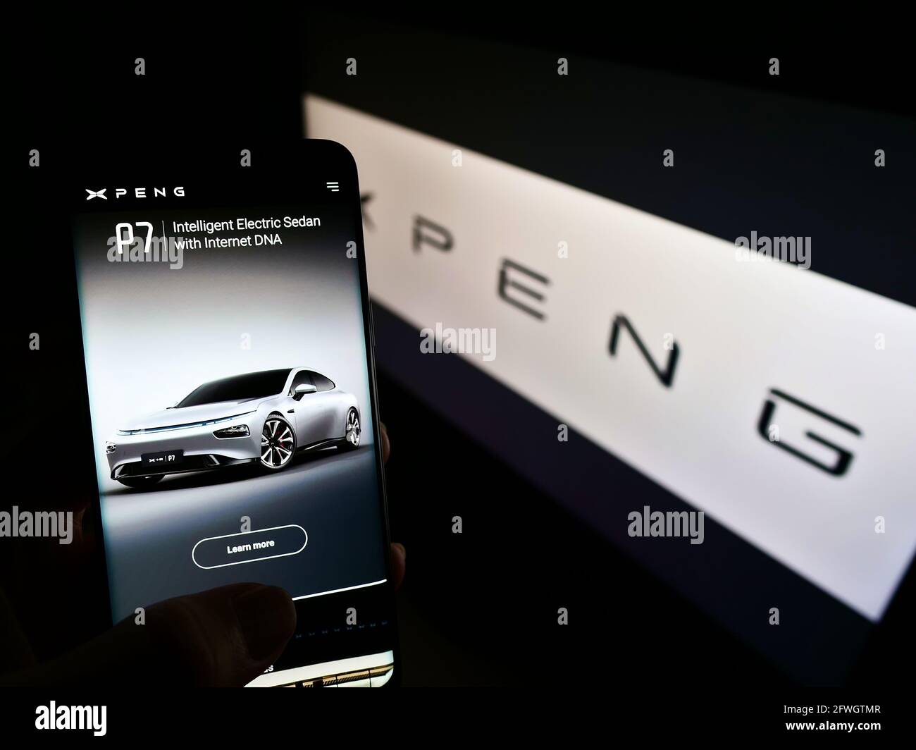 Person holding smartphone with webpage of Chinese electric car manufacturer Xiaopeng Motors on screen with logo. Focus on center of phone display. Stock Photo