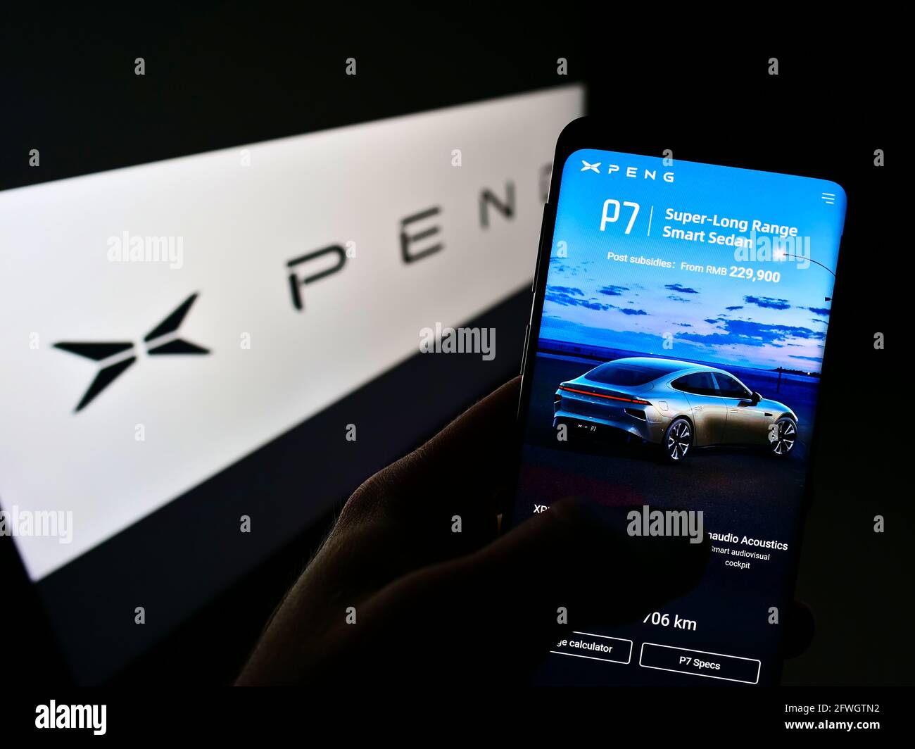 Person holding mobile phone with webpage of Chinese electric car manufacturer Xiaopeng Motors on screen with logo. Focus on center of phone display. Stock Photo