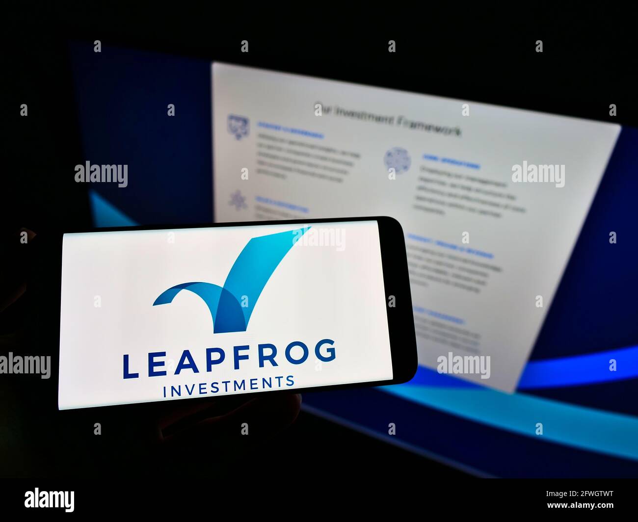 Person holding smartphone with logo of private equity firm LeapFrog Investments on screen in front of website. Focus on phone display. Stock Photo
