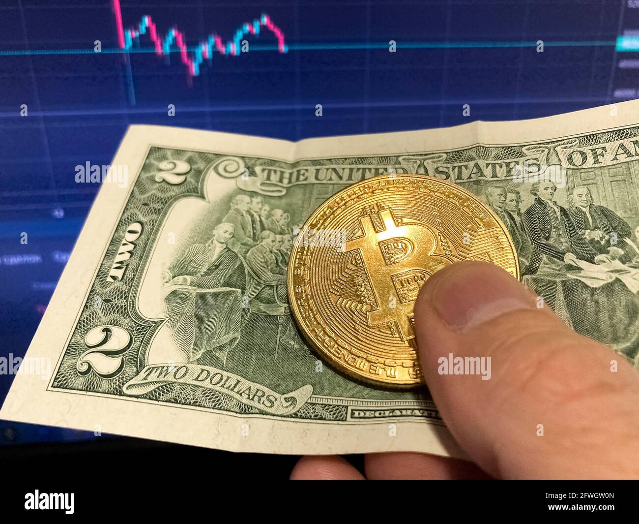 Bitcoin coin on paper bill two Dollars. Selective focus. The electronic schedule of bitcoin, volume trades Stock Photo