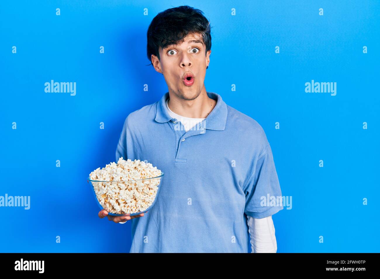 Handsome hipster young man eating popcorn scared and amazed with open