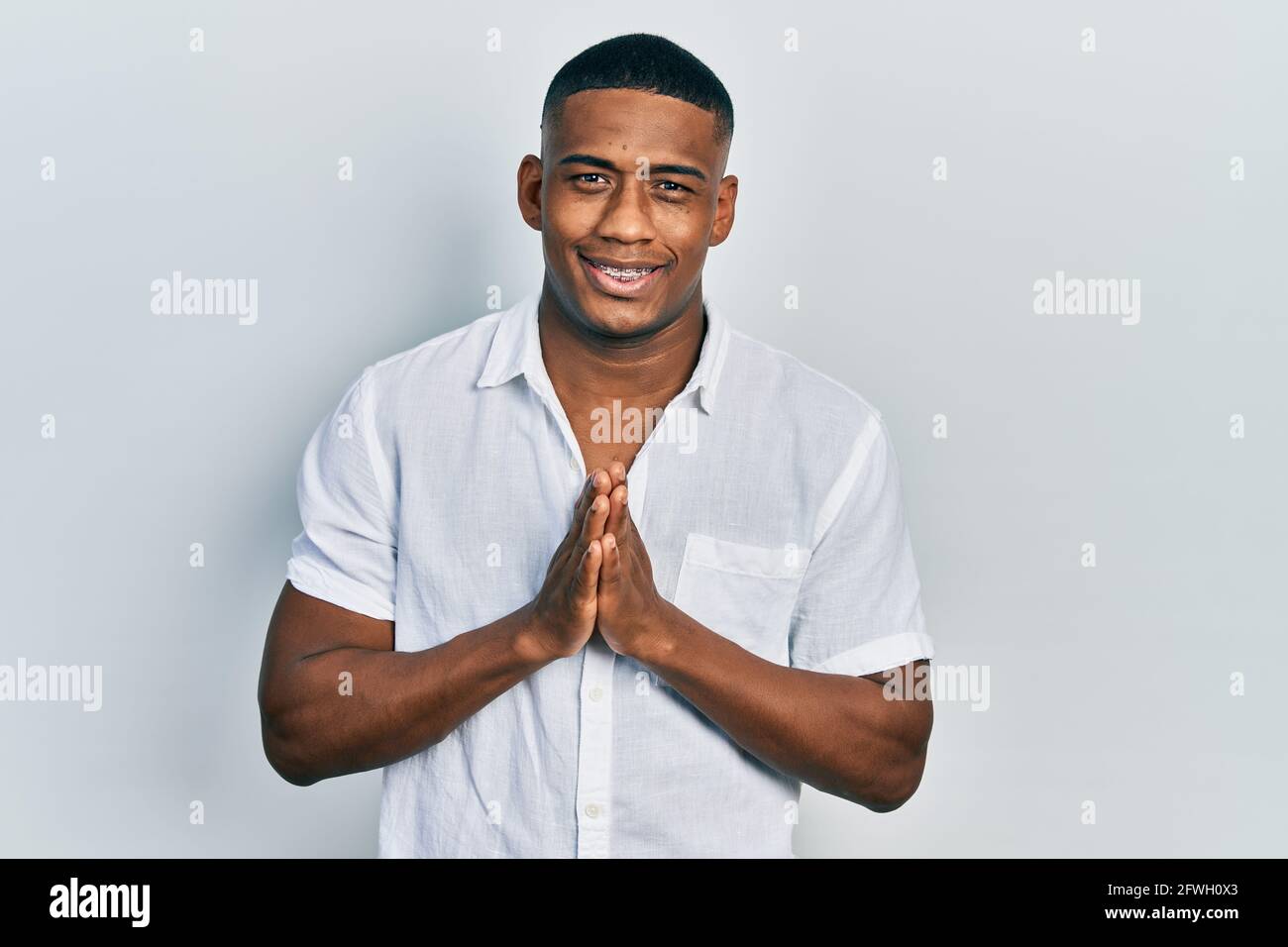 Young black man wearing casual white shirt praying with hands together ...