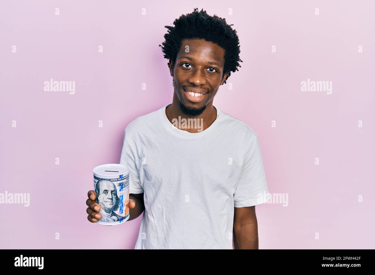 Young african american man holding piggy bank looking positive and ...