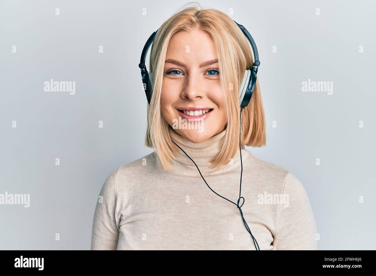 Young blonde woman listening to music using headphones looking positive ...