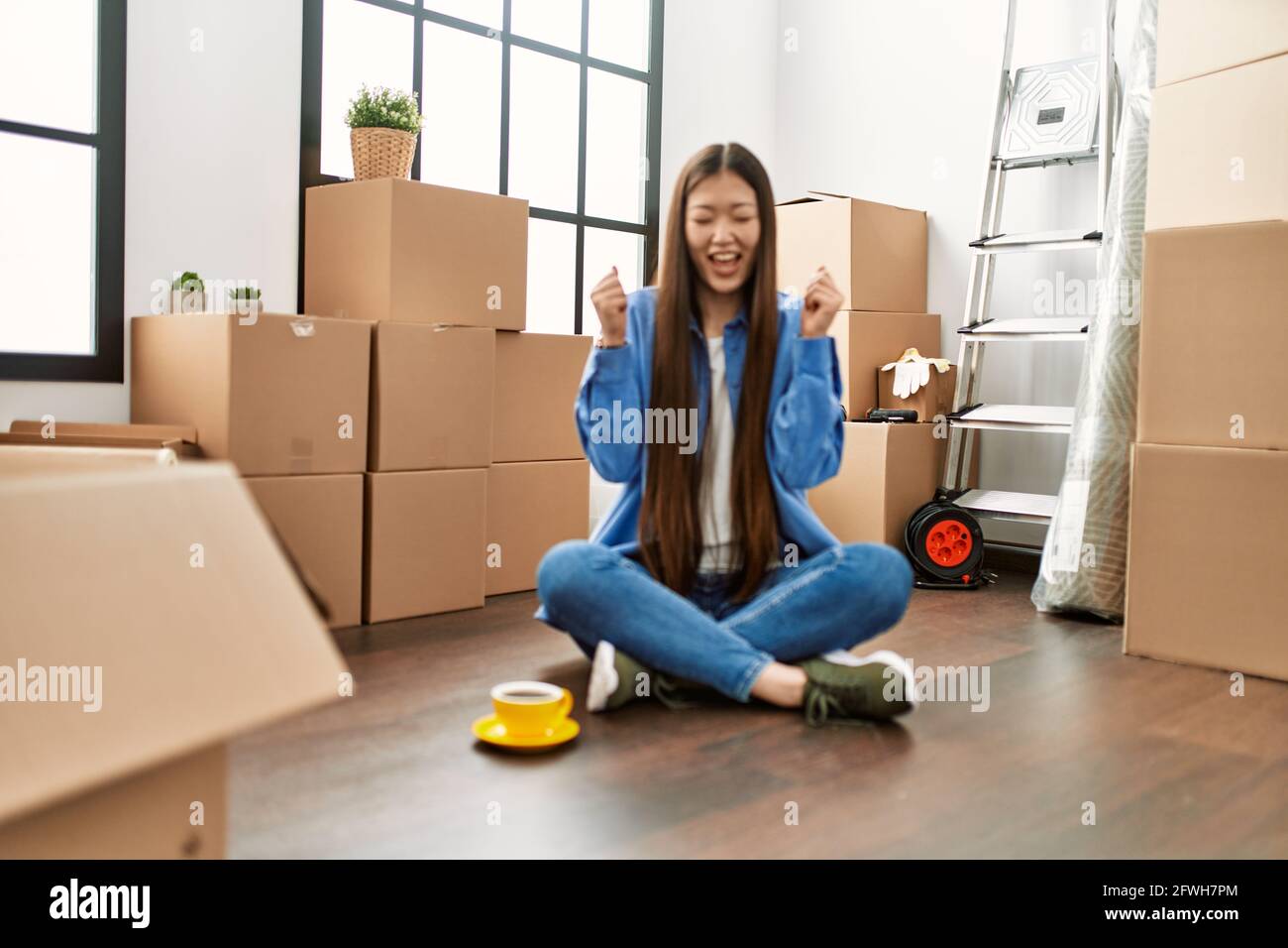 Young chinese girl sitting on the floor at new home excited for success ...