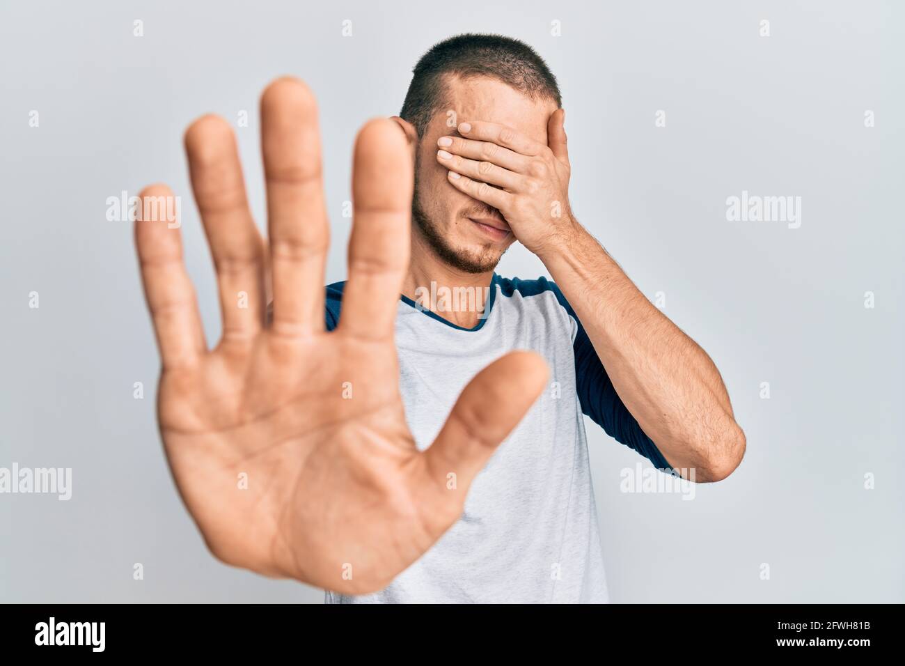 Hispanic young man wearing casual clothes covering eyes with hands and ...