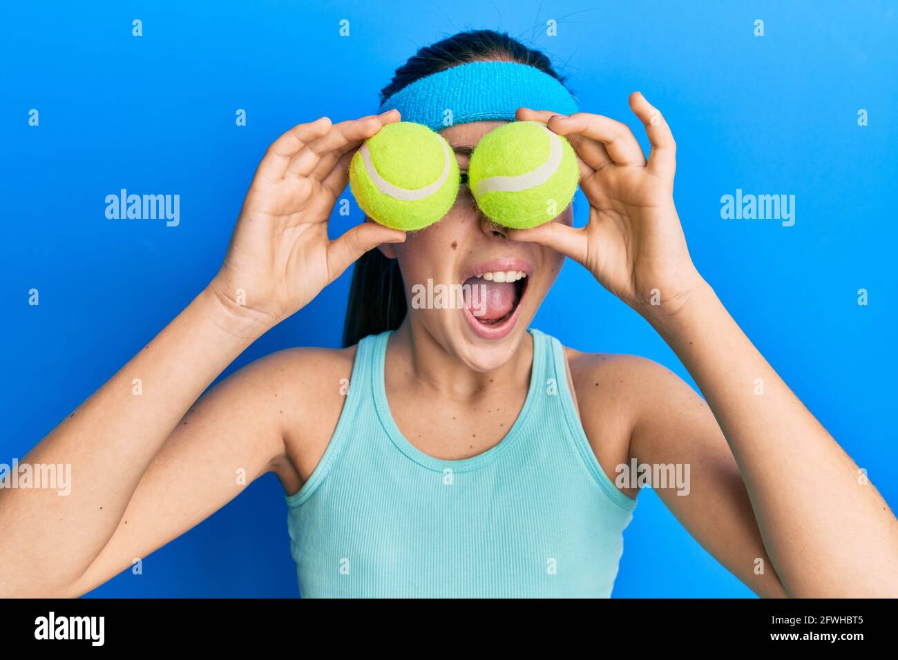 Beautiful brunette little girl holding tennis ball close to eyes angry