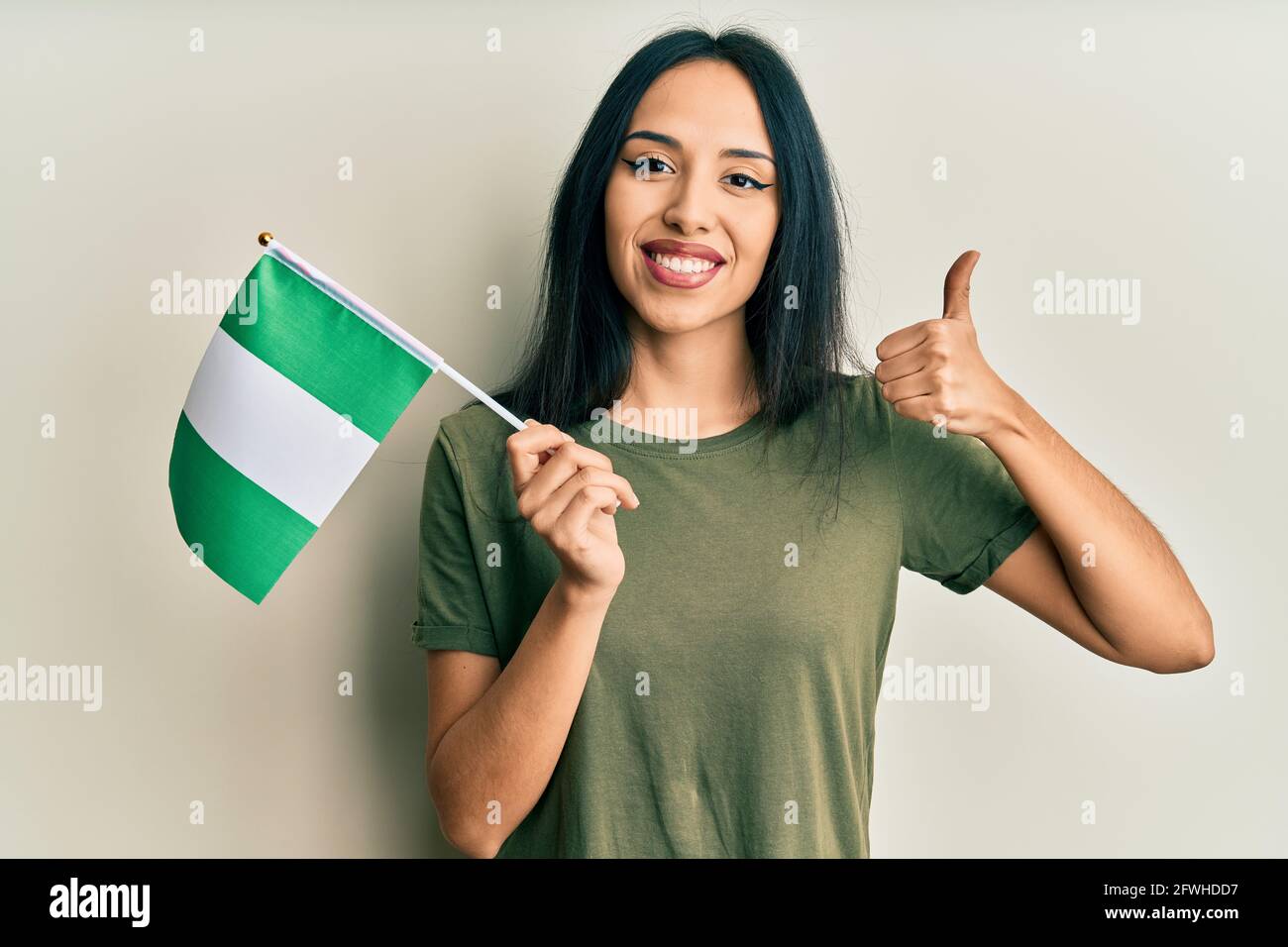 Young hispanic girl holding nigeria flag smiling happy and positive ...