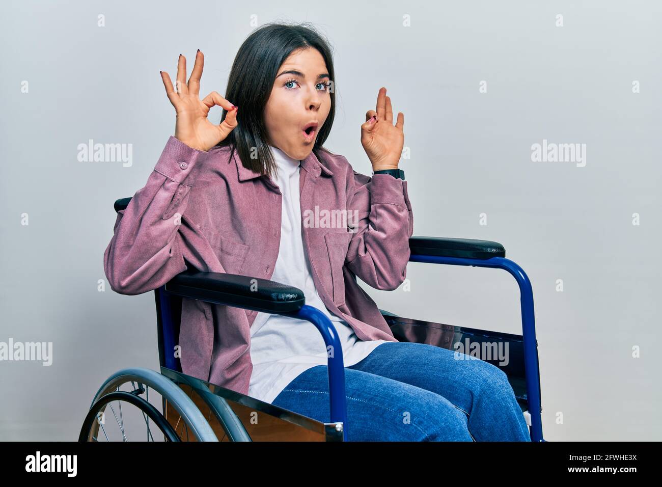 Young brunette woman sitting on wheelchair looking surprised and ...