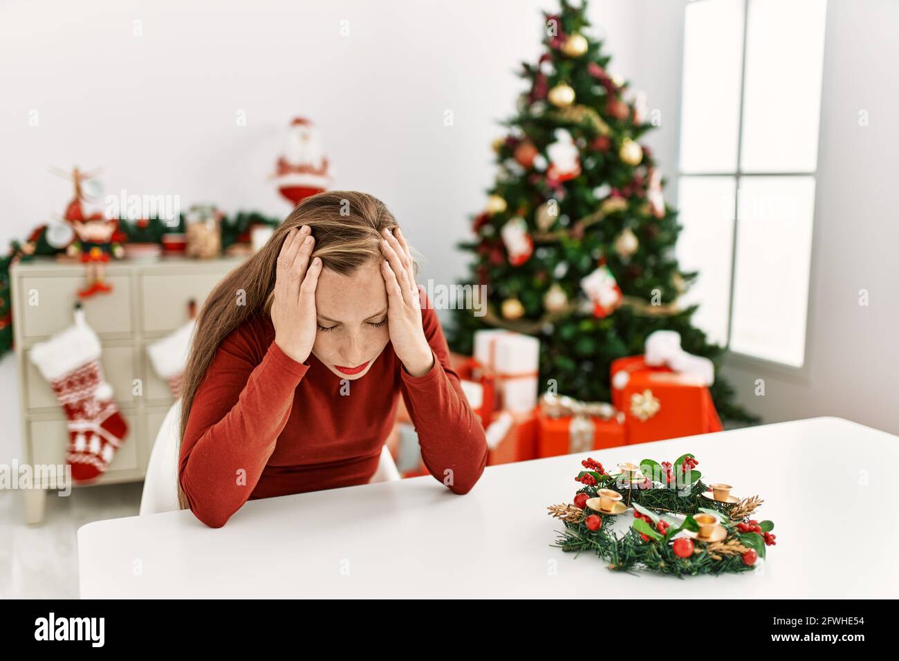 Caucasian young blonde woman sitting on the table by christmas tree