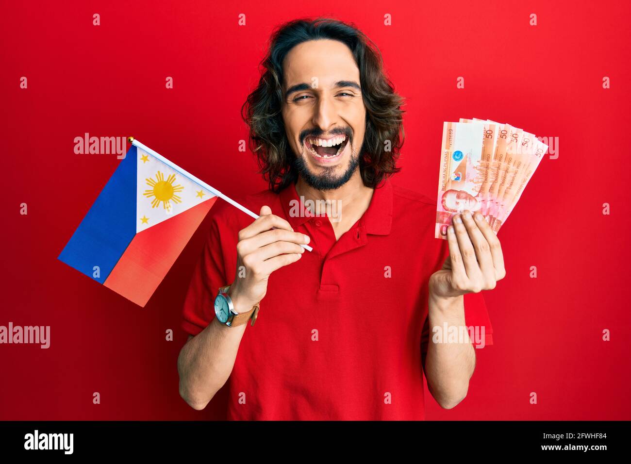 Young hispanic man holding philippines flag and pesos banknotes smiling