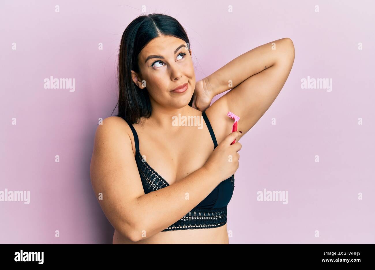 Beautiful woman shaving armpit hair with razor smiling looking