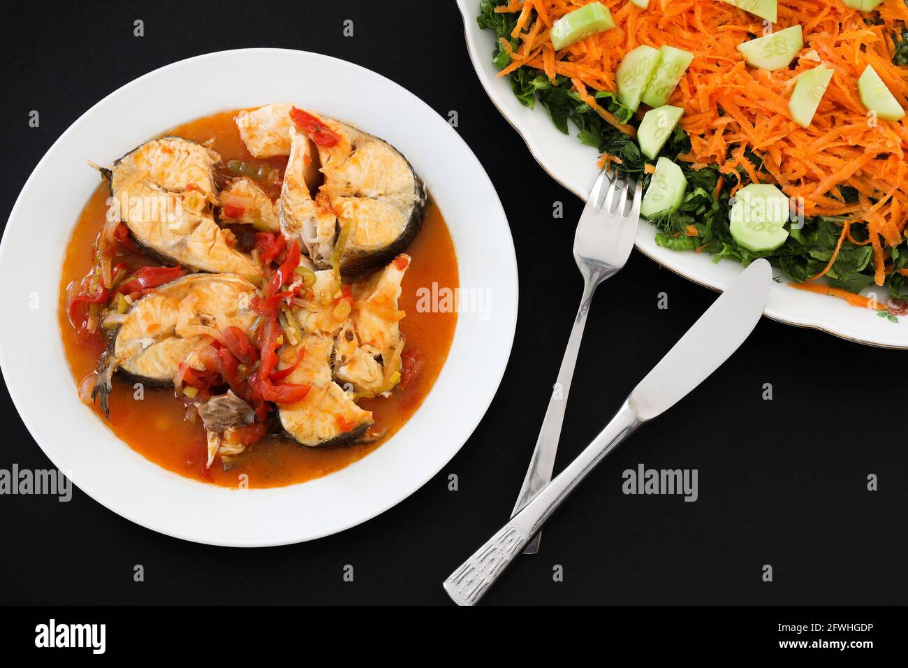 Steamed sea bass in sauce served on plate with green salad on black