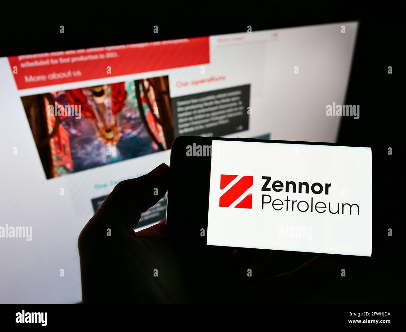 Person holding mobile phone with logo of British oil and gas company Zennor Petroleum Ltd. on screen in front of web page. Focus on phone display. Stock Photo