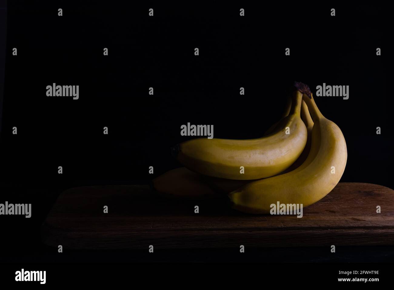 several bananas on a wooden board on a dark background. Stock Photo