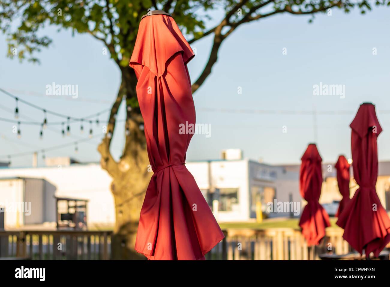 Closed red patio umbrellas on an outdoor patio deck at sunset Stock
