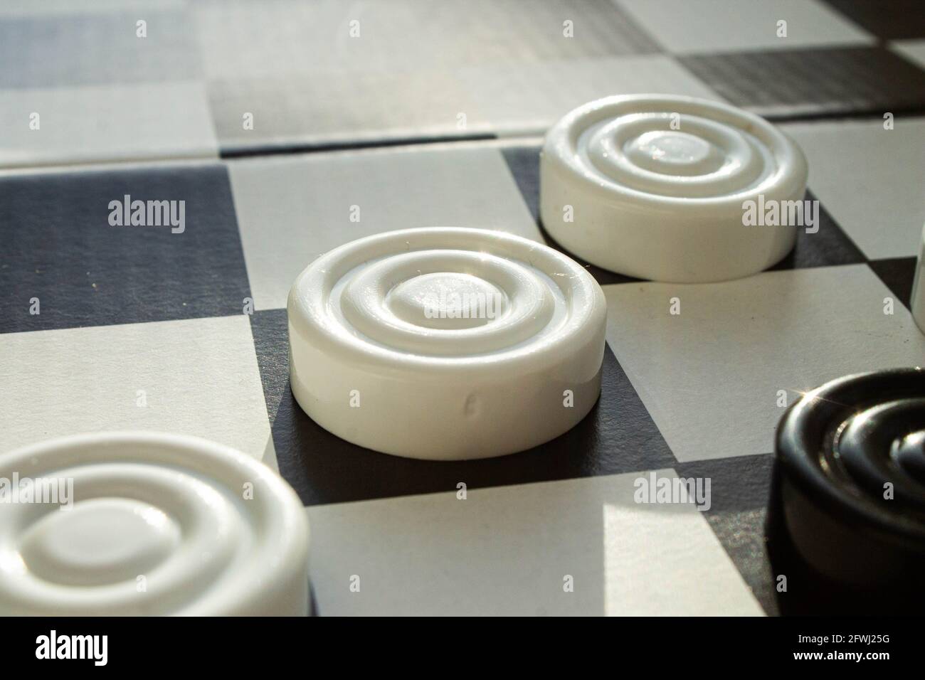 Board game of checkers. Black and white chips for the game. Chess field. Checkers move close-up. Checker in hand. Stock Photo