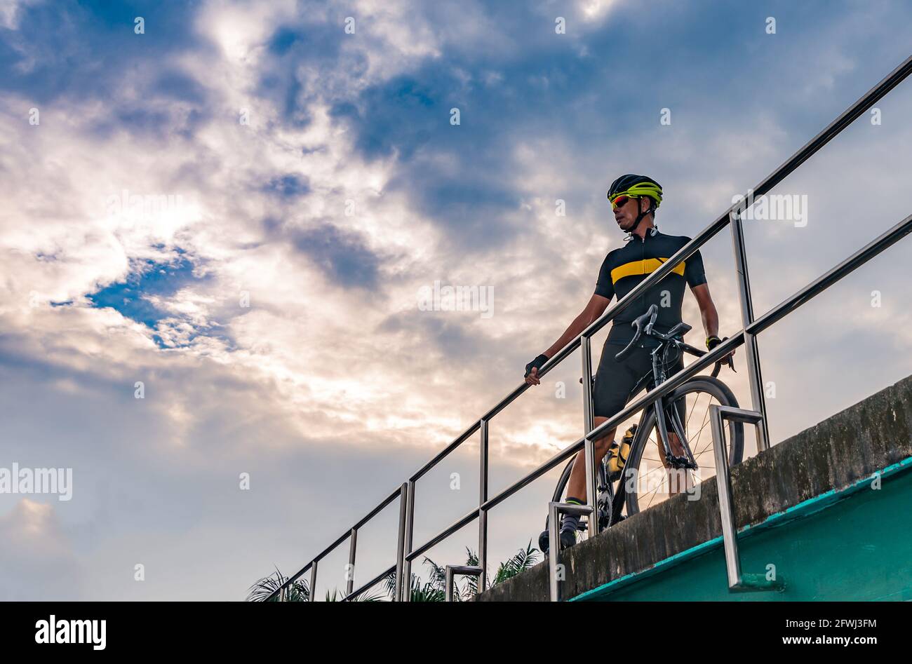 Portrait of Asian cyclist with sport bicycle posing on the bridge, bird eye view, sunset image, blank space for text. Stock Photo