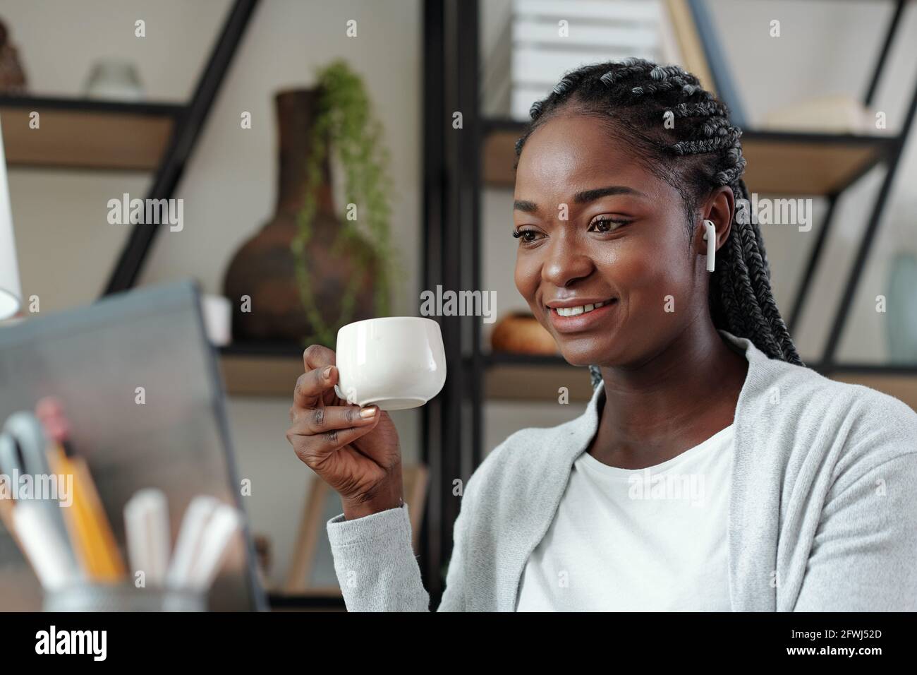 Portrait of joyful young businesswoman drinking coffee and video calling colleagues to discussing company development Stock Photo