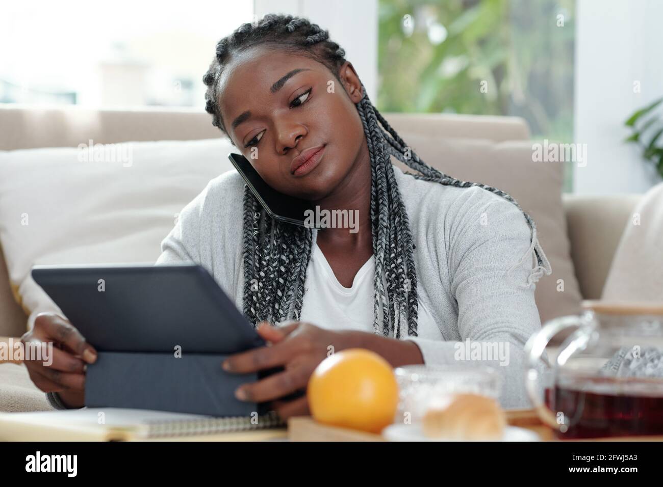 Serious pretty woman talking on phone and reading document or watching presentation on tablet computer Stock Photo