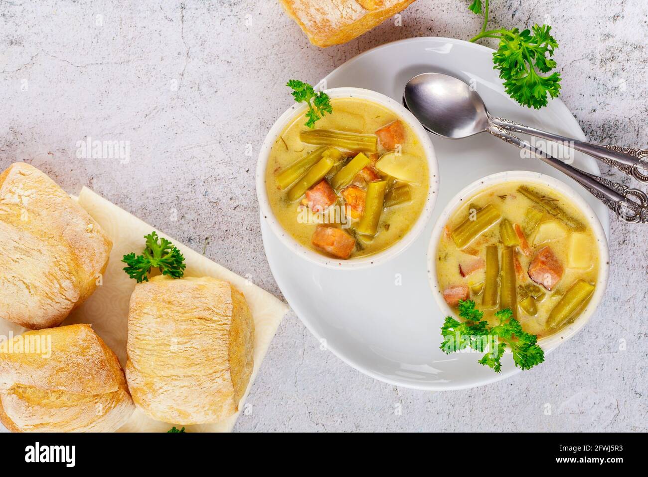 Homemade creamy vegetable soup on white bowl with dinner roll and spoon ...