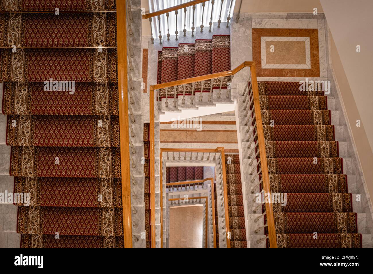 Downward view of spiral staircase with several flights decorated with carpets. Stock Photo