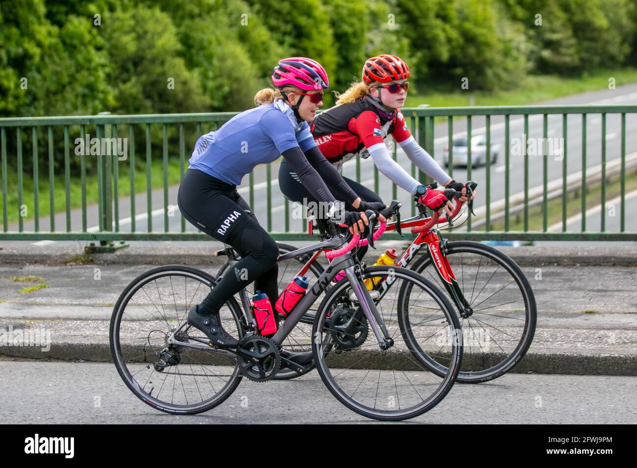 Two female cyclists riding LIV sports road bike wearing Rapha clothing, on countryside route crossing motorway bridge in rural Lancashire, UK Stock Photo