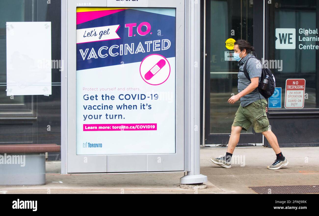 Toronto, Canada. 22nd May, 2021. A man wearing a face mask walks past a poster displaying information about the COVID-19 vaccination in Toronto, Canada, on May 22, 2021. About 50.08 percent of Canada's population were administered with the first dose of COVID-19 vaccine and 4.3 percent with second dose as of Saturday afternoon, according to CTV. Credit: Zou Zheng/Xinhua/Alamy Live News Stock Photo
