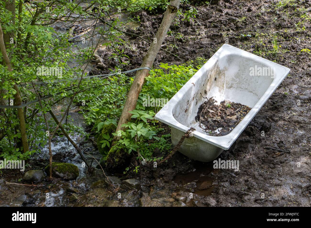 An old tub chained to a tree by a stream. Natural bathroom. Stock Photo