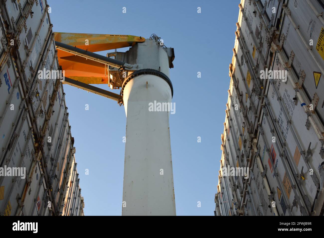 View on cabin of the ship crane in gap between rows of white colors containers stacked on each other. Stock Photo