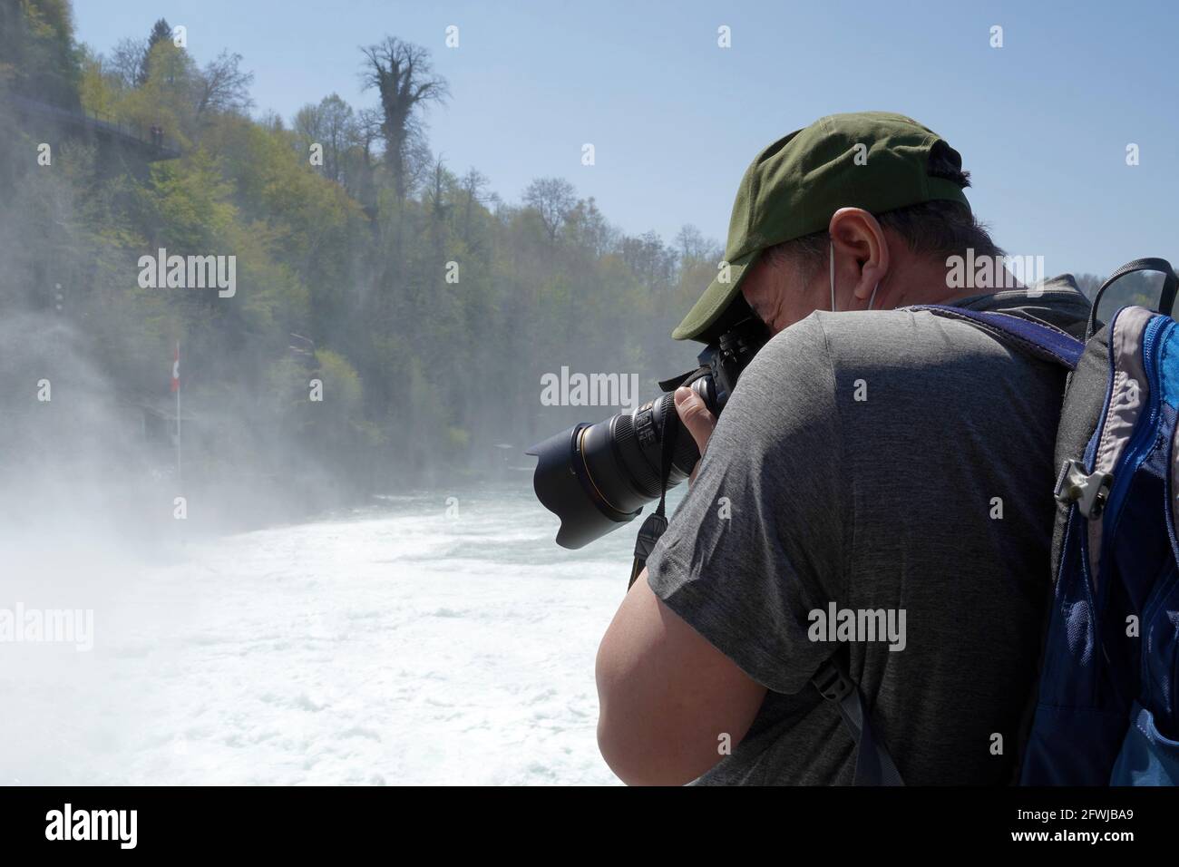 Man taking photograph of a Rhine Fall waterfall in Switzerland with a camera. Stock Photo