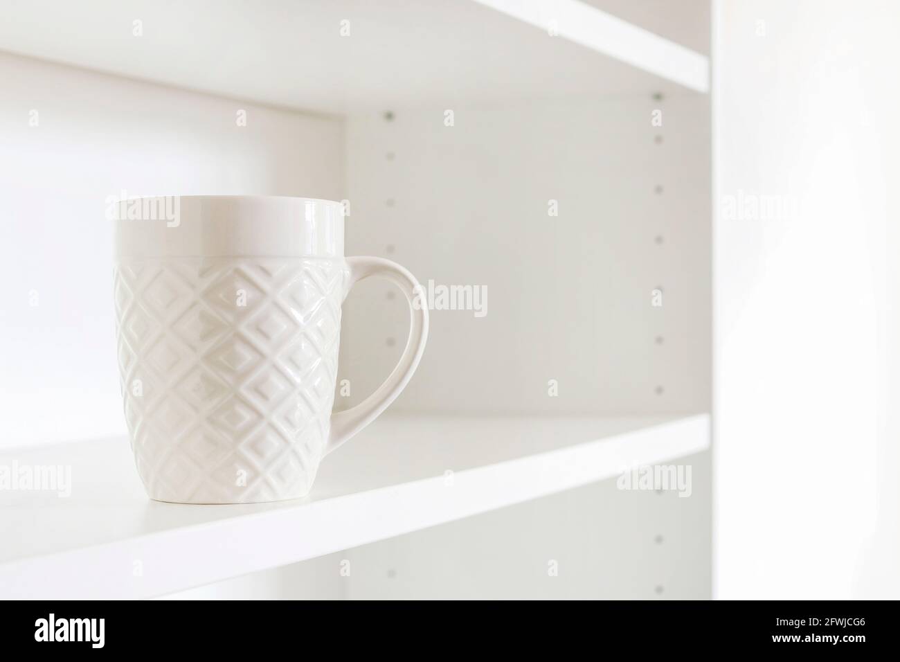 A white ceramic mug standing on an empty shelf. Home cleaning Stock Photo